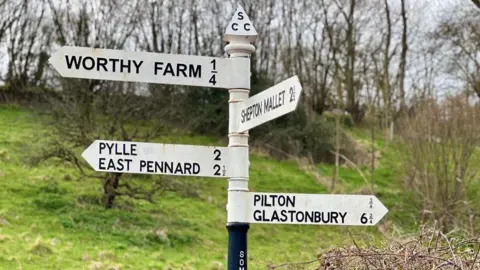 A white signpost signalling the direction and distance to Worthy Farm, Pilton and Glastonbury