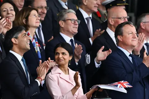 PA Rishi Sunak and his wife, Akshata Murty, stand in front of Keir Starmer at Normandy D-Day event