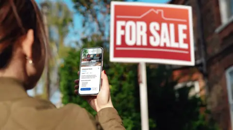 getty Woman looking for property to buy via real estate website on smartphone