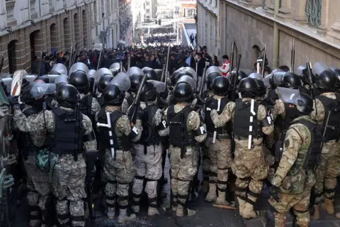 Luis Gandarillas/EPA Military police line up in front of a crowd of densely packed supporters of Bolivian President Luis Arce during a protest against military personnel trying to enter the government headquarters in La Paz, Bolivia, 26 June 2024