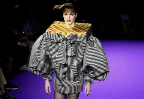 Stephanie Lecocq/REUTERS A model presents a creation of a black and white stripe jacket with puff sleeves, accentuated shoulders which a neck piece resembling a chess board,  for the Haute Couture Fall/Winter 2024-2025 collection show for fashion house Viktor & Rolf in Paris, France