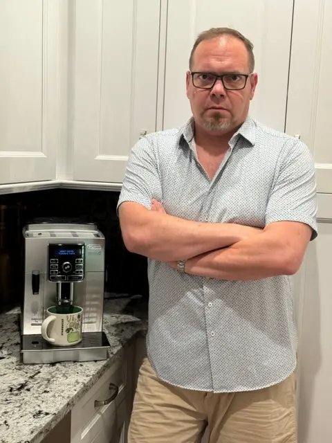 Andrew Buckley Andrew Buckley standing with arms crossed in his kitchen next to his coffee machine