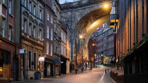 Getty Images An empty street lined with tall buildings leading up to a viaduct 