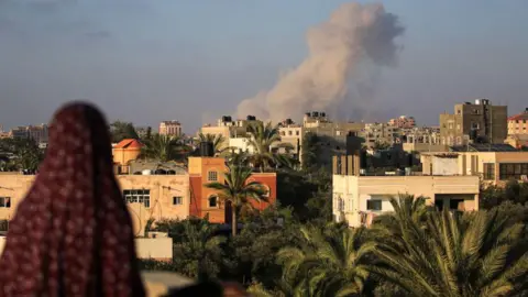 AFP A Palestinian woman watches as smoke billows following an Israeli strike south of Gaza City, in the town of al-Zawaida, in the central Gaza Strip (11 June 2024)