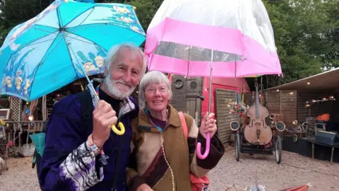 Handout Graham and Judy Cole standing at Glastonbury Festival holding a blue and pink umbrella