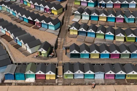 Dan Kitwood/Getty Images Aerial photo showing a man sunbathing in front of a row of beach huts on June 26, 2024 in Walton-On-The-Naze, England