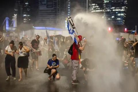 Reuters Demonstrators take cover from the Israeli police's water cannon, at a demonstration against Prime Minister Benjamin Netanyahu's government and a call for the release of hostages in Gaza, amid the Israel-Hamas conflict, in Tel Aviv