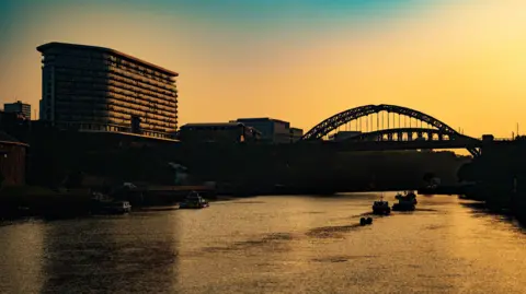 Getty Images A building and bridge silhouetted against a yellow sunrise