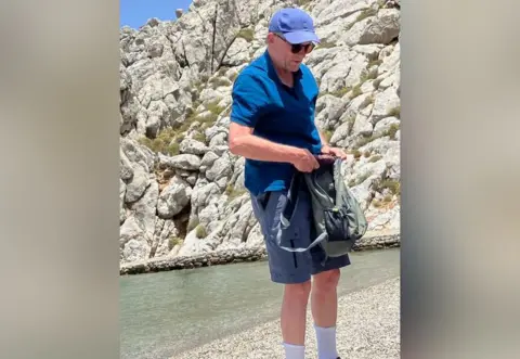 Facebook Michael Mosley on a beach, he is wearing a blue cap, sunglasses and a blue Polo shirt