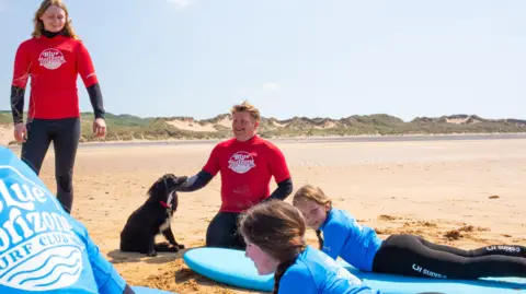 Ollie Bird Ariel, the formerly six-legged dog, with members of the surf club on the beach