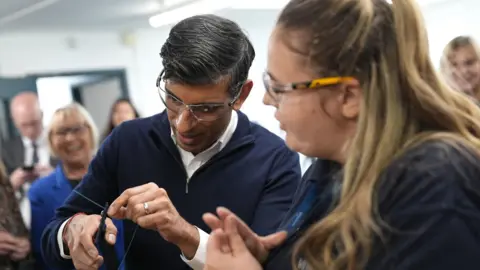 PA Prime Minister Rishi Sunak is shown how to splice a wire by a field service engineer apprentice