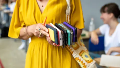 Getty Women in yellow dress holds multiple cell phones in her hands