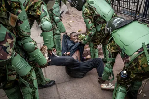 LUIS TATO/AFP A man, wearing black, reacts on the floor as Kenya Police officers, wearing riot uniforms, arrest him while stopping people from gathering for a planned demonstration in downtown Nairobi, on June 27, 2024.