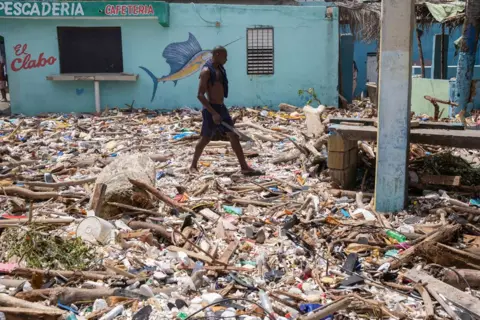 Orlando Barria/EPA A man wearing shorts walks along the beach of Manresa, covered with debris, following the passage of Hurricane Beryl, in Santo Domingo, Dominican Republic, 3 July 2024.