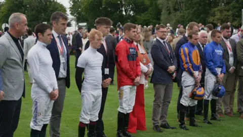 Shaun Whitmore/BBC Jockeys and others at Newmarket holding silence