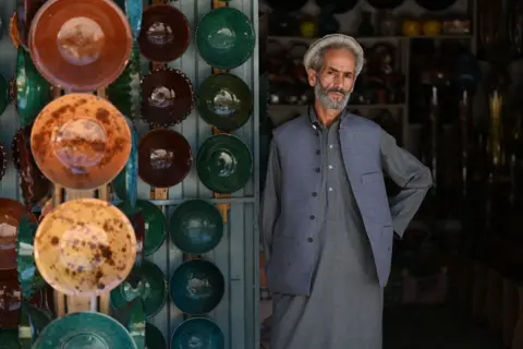 Getty Images An Afghan vendor waits for customers at his shop selling clay bowls at a market in Istalif district in northwest of Kabul province on July 3, 2023