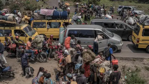 AFP People gather at a busy road while carrying some of their belongings as they flee the Masisi territory following clashes between M23 rebels and government forces, at a road near Sake, DR Congo - February 2024