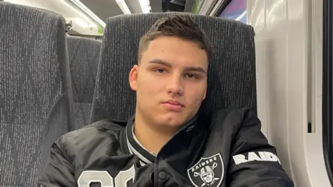 Family photograph Narcis Titianu, pictured on a train. He is wearing a sports jacket, has short dark hair and is smiling at the camera. 