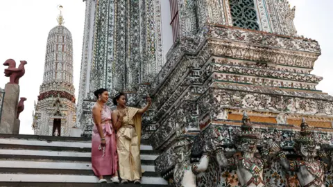 Getty Images Tourists in Thai traditional dress take a selfie at Wat Arun on Vesak Day in Bangkok, Thailand on May 22, 2024. 