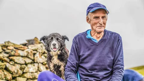 Stephen Wilson Joss Naylor sitting on a Lake District fell, accompanied by a dog