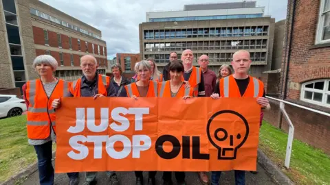 Oli Constable/BBC Just Stop Oil protesters with a banner outside court