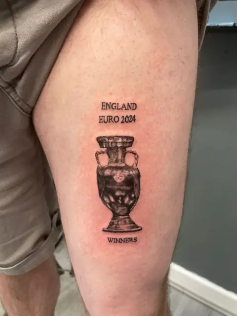 Jack Wilkinson/PA Media Man tattoos trophy and words: "England Euro 2024 Winners" on his leg ahead of the final.