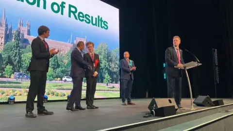 Shariqua Ahmed/BBC Sam Carling shakes hands with the defeated Conservative candidate after the result is announced