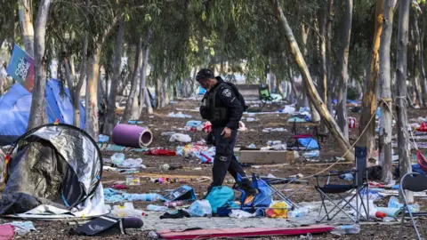 EPA An Israeli officer walks at the site of the Supernova music festival, in southern Israel, after the killing of hundreds of Israeli civilians by Hamas-led gunman (17 October 2023)