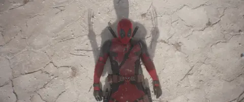 Disney Deadpool knocked to the ground as the shadow of Wolverine's claws tower over him