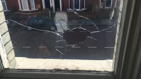 A hole smashed through the centre of a window. The picture is taken from inside and looks down on a residential street in Jesmond.