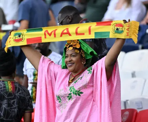 MUSTAFA YALCIN/GETTY IMAGES A woman in a pink dress waves a Mali flag at a stadium in Paris, France - Thursday 25 July 2024