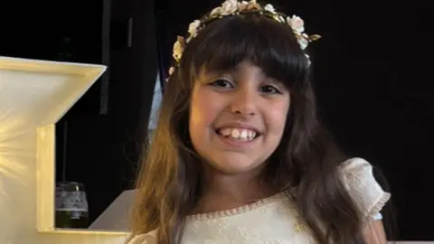 Family photograph Alice Dasilva Aguiar smiles in a formal dress while wearing a floral garland