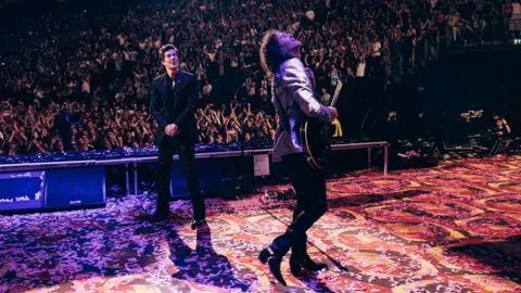 Chris Phelps Brandon Flowers and Dave Keuning on stage looking up at the screen