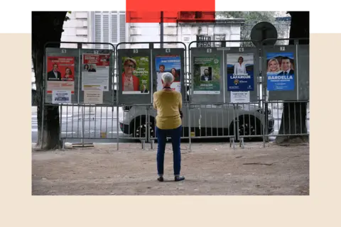 Getty Images A woman looks at election posters next to a polling station during the first round of parliamentary elections in Pau, south-western France