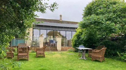 Hotel garden with lawn and building made from cotswold stone and glass