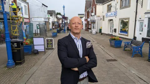 Councillor Stewart Golton in a blazer stood in the middle of a high street