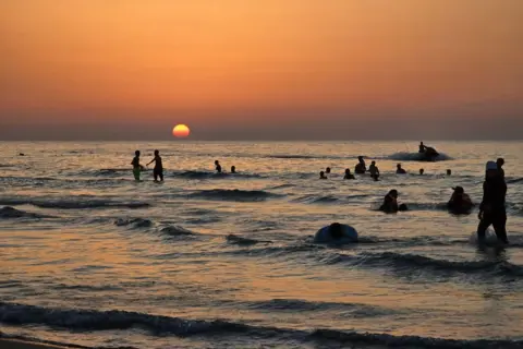 MAHMUD TURKIA/AFP People swim in the sea at sunset in Qarabuli, Libya - Saturday 20 July 2024