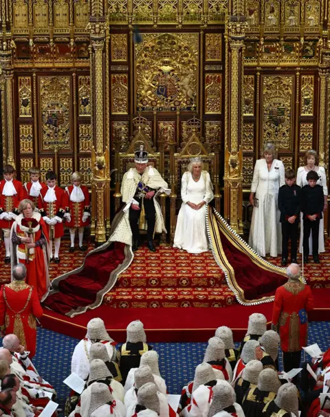 HENRY NICHOLLS/AFP King Charles III, wearing the Imperial State Crown and the Robe of State, sits alongside Queen Camilla before reading the King's Speech from the Sovereign's Throne in the House of Lords chamber, during the State Opening of Parliament, at the Houses of Parliament, in London