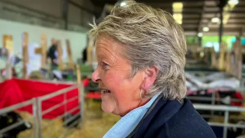 woman in a sheep shed with shorter hair, almost a mullet