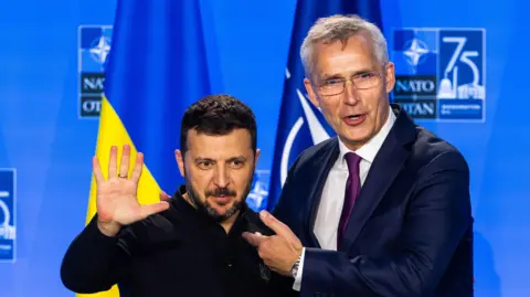 EPA President of Ukraine Volodymyr Zelensky embraces Jens Stoltenberg in front of a Ukrainian flag next to a Nato flag