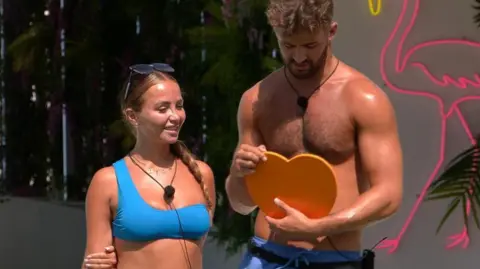 ITV/REX/Shutterstock Ciaran and Nicole standing beside each other in swimwear and holding a heart shaped 