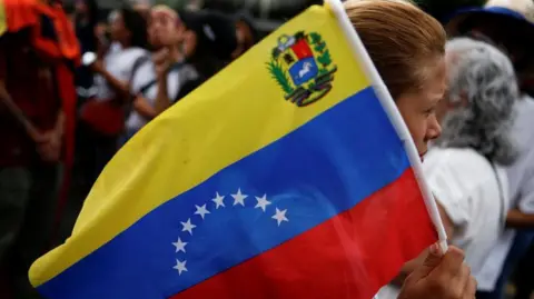 Reuters A demonstrator holds a Venezuelan flag as people gather to protest election results that awarded Venezuela's President Nicolas Maduro with a third term, in Caracas, Venezuela July 30, 2024. 