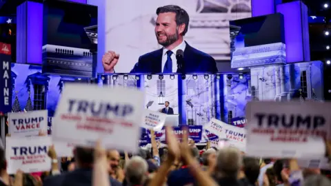 EFE JD Vance seen on a big screen as supporters carrying signs reading TRUMP