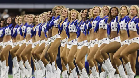 Getty Images Smiling members of the Dallas Cowboys Cheerleaders standing in their uniforms in a row