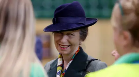 Reuters Princess Anne wearing a dark purple hat smiling