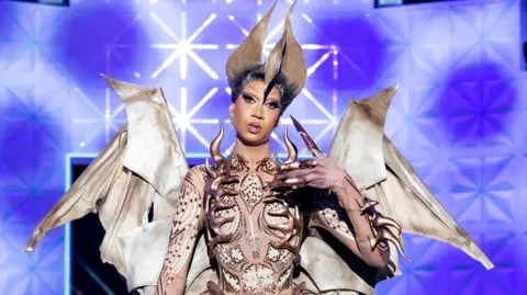 BBC/World of Wonder/Guy Levy Tia Kofi on the runway for Ru Paul's Drag Race UK vs The World, series two. Tia wears a look inspired by a teradactyl, complete with wings and a spikey bodice.