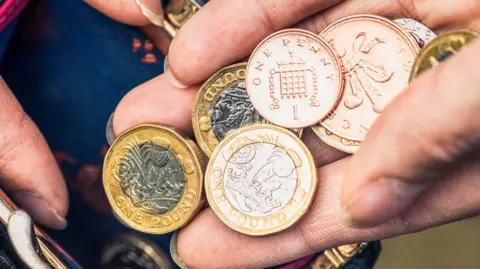 Getty Images Selection of different coins in someone's hand, held above a purse