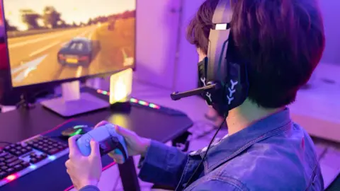 Getty Images Male Gamer Playing Driving Game with Game Controller in Neon Game Room