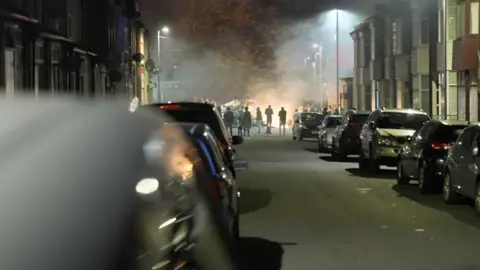 BBC People gather around a fire on a street in Harehills