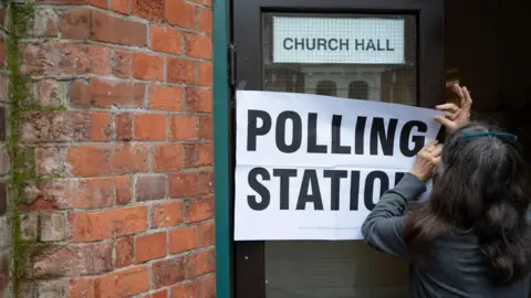 Getty Images Woman puts up a sign reading "polling station" on a church hall